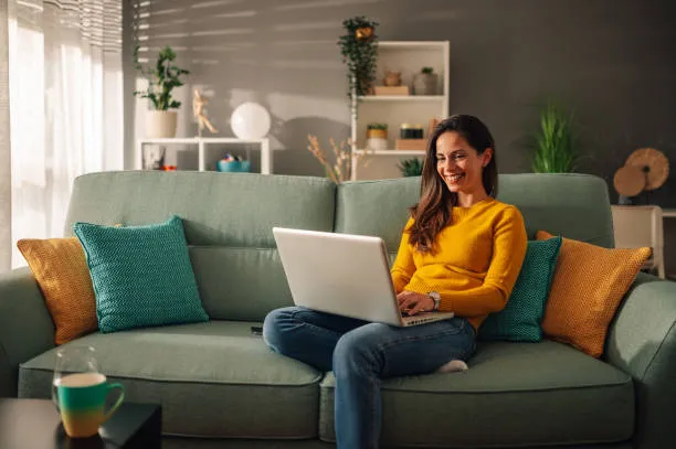 Femme souriante utilisant un ordinateur portable sur un canapé