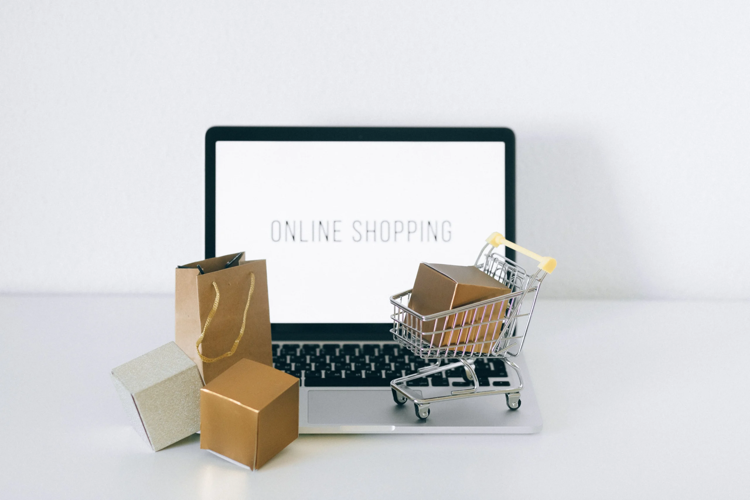 Ordinateur portable affichant Online Shopping avec un mini caddie et des petits colis carton pour représenter la création d'un site e-commerce.