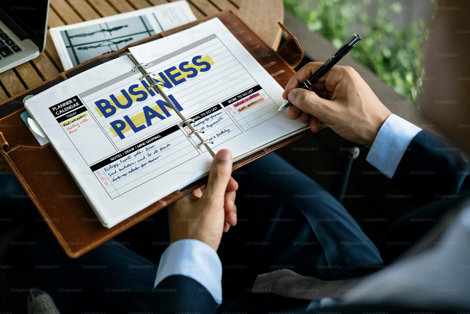 Personne tenant un bloc-notes sur lequel est écrit Business Plan avec un stylo.
