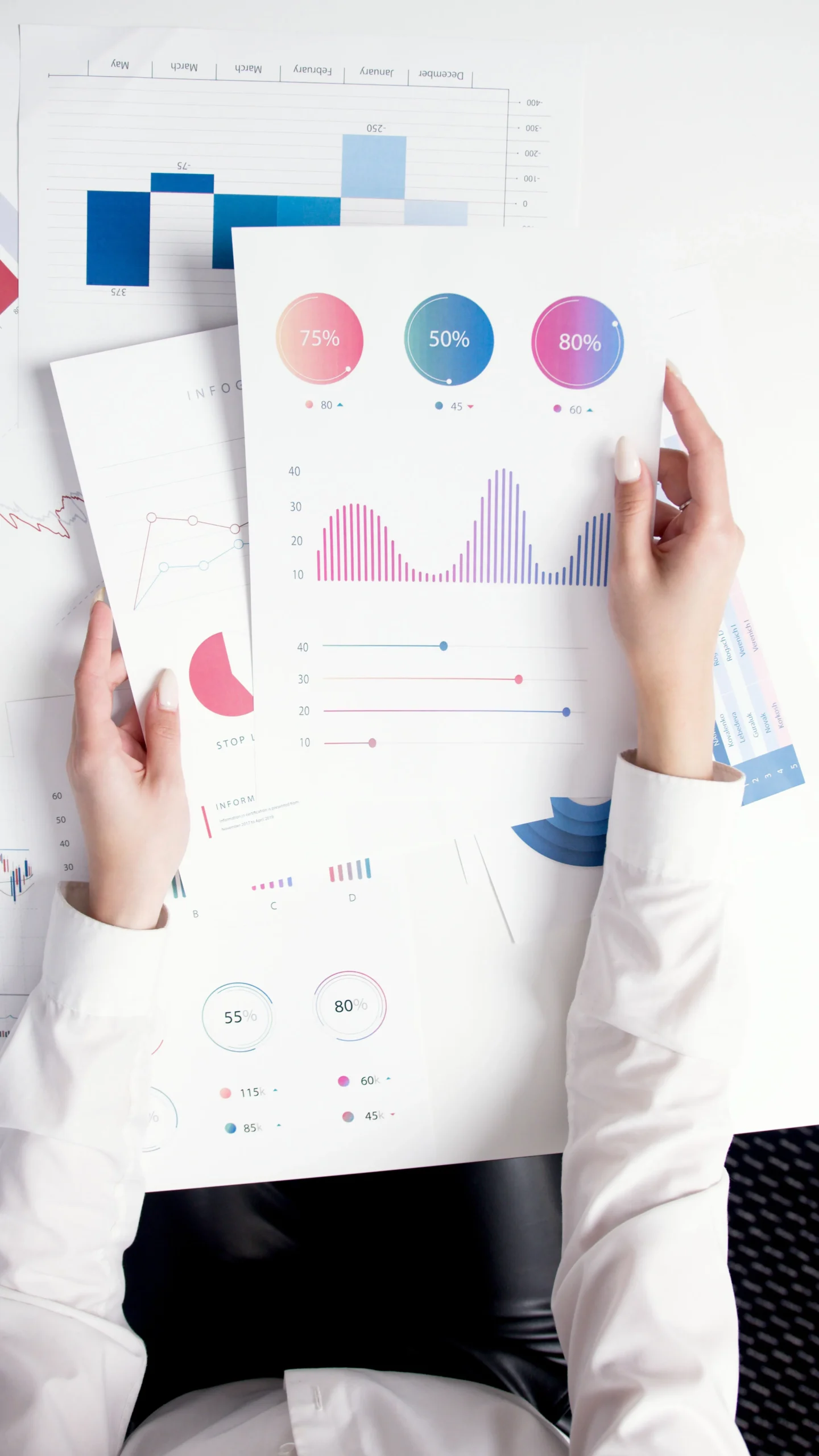 Une personne en chemise blanche tenant des rapports imprimés contenant des graphiques et des statistiques de ventes.