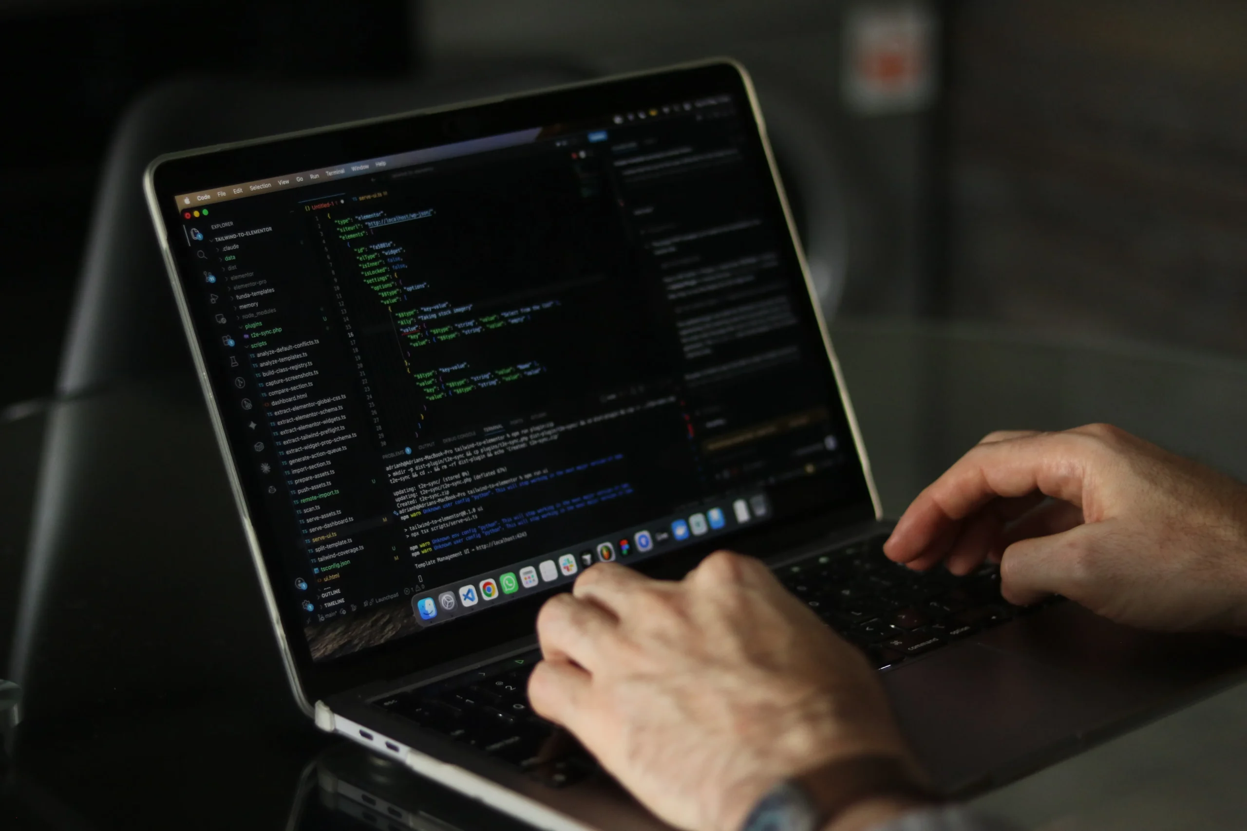 Mains sur le clavier d'un ordinateur portable affichant des scripts de programmation.