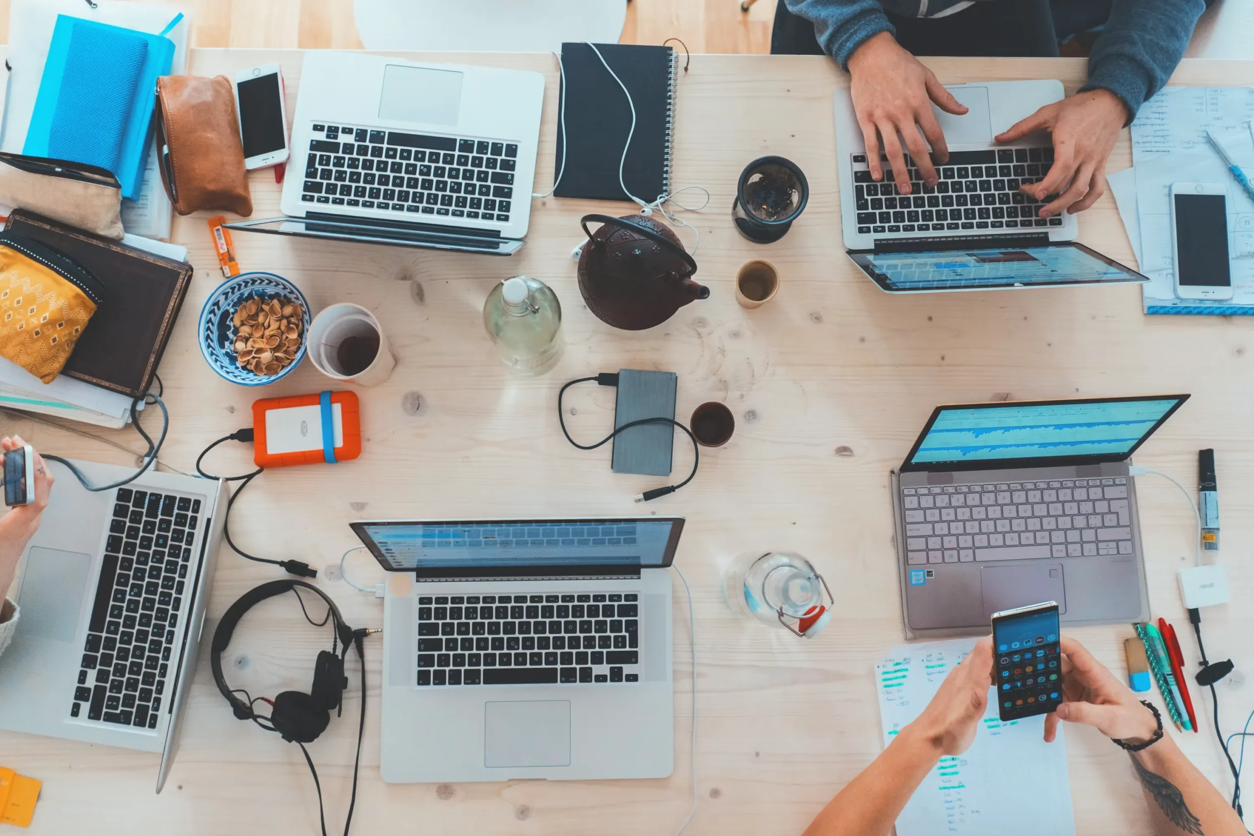 Vue de haut d'une table de réunion entourée de collaborateurs avec ordinateurs portables et téléphones.